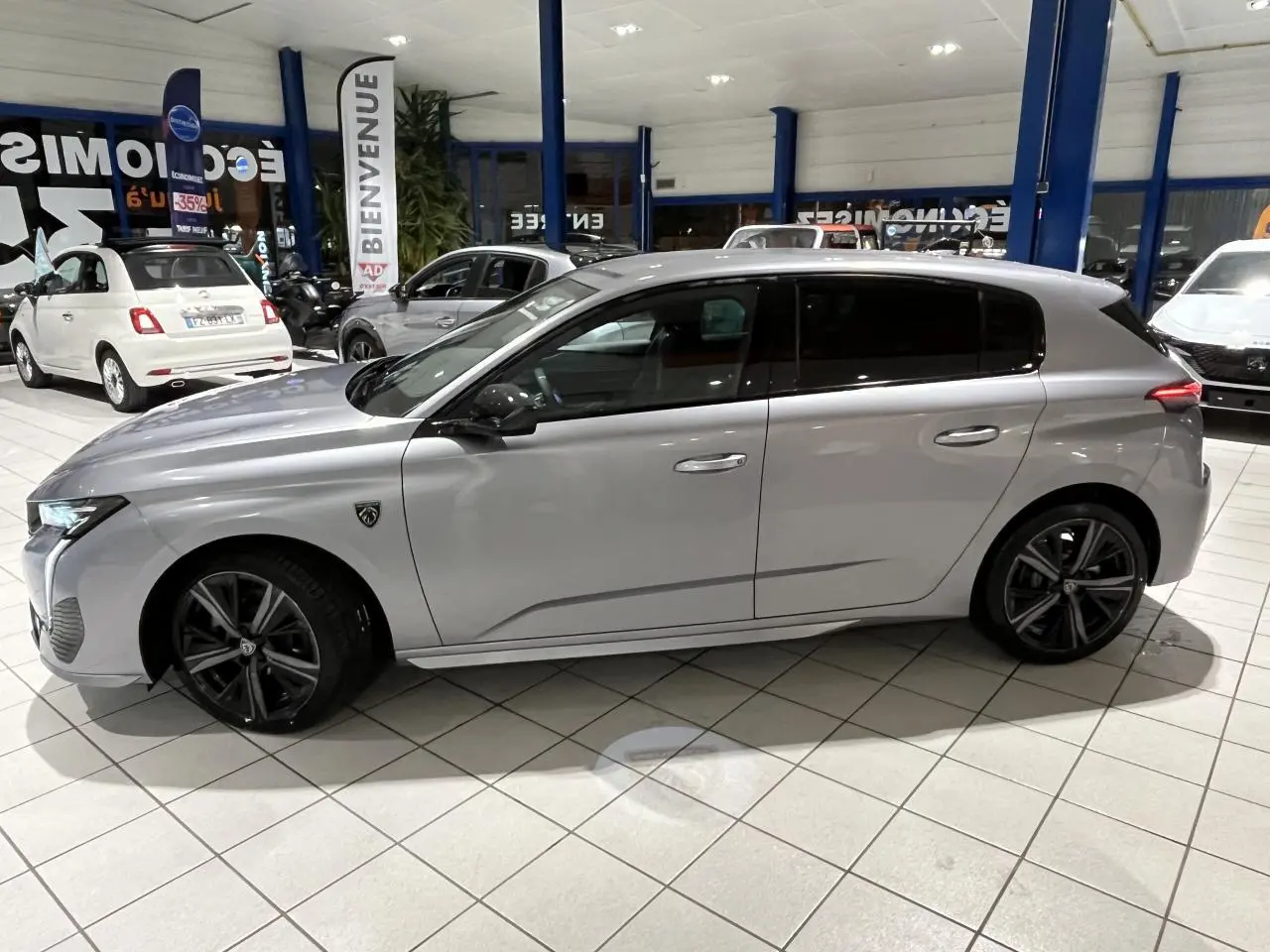 Peugeot 308 Gris Artense vue de profil côté gauche en intérieur, jantes alliage noires et toit noir brillant.
