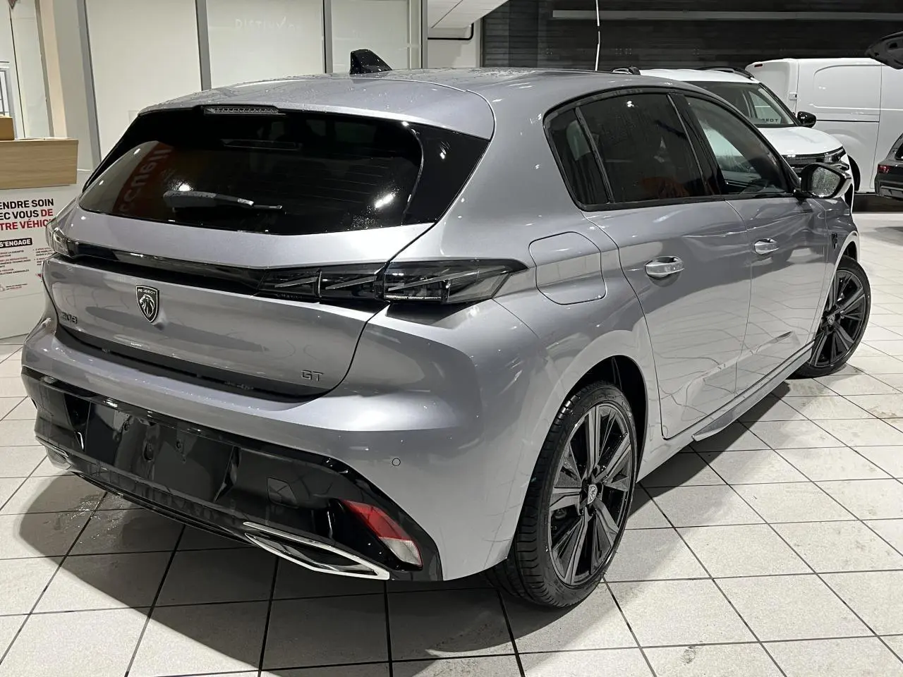 Vue 3/4 arrière droit d’une Peugeot 308 GT 2024 gris Artense avec feux arrière noirs brillants et jantes alliage 18 pouces.