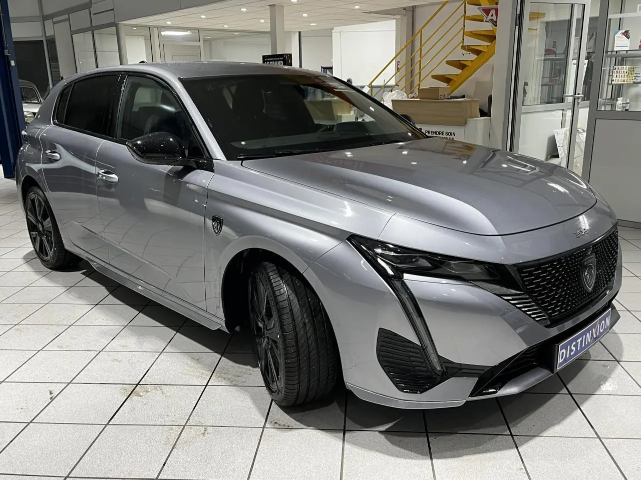 Peugeot 308 GT gris Artense vue 3/4 avant en intérieur avec calandre noire et jantes alliage 18 pouces.