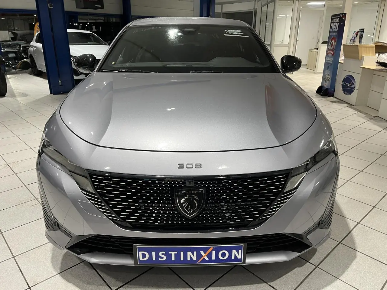 Vue avant frontale d'une Peugeot 308 gris Artense avec calandre noire brillante et logo lion central.
