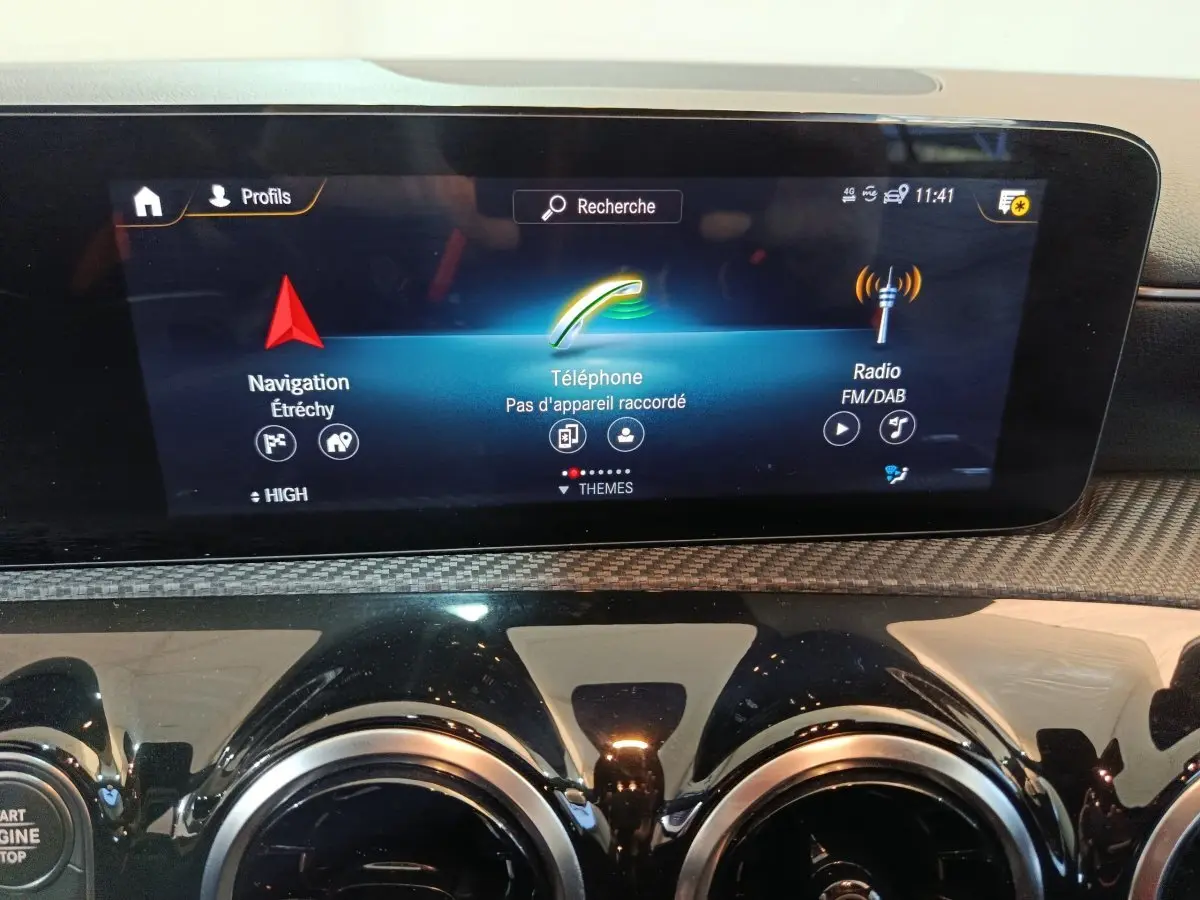 Vue rapprochée de l’écran tactile central et des aérateurs ronds noirs du tableau de bord d’une Mercedes Classe A bleu.