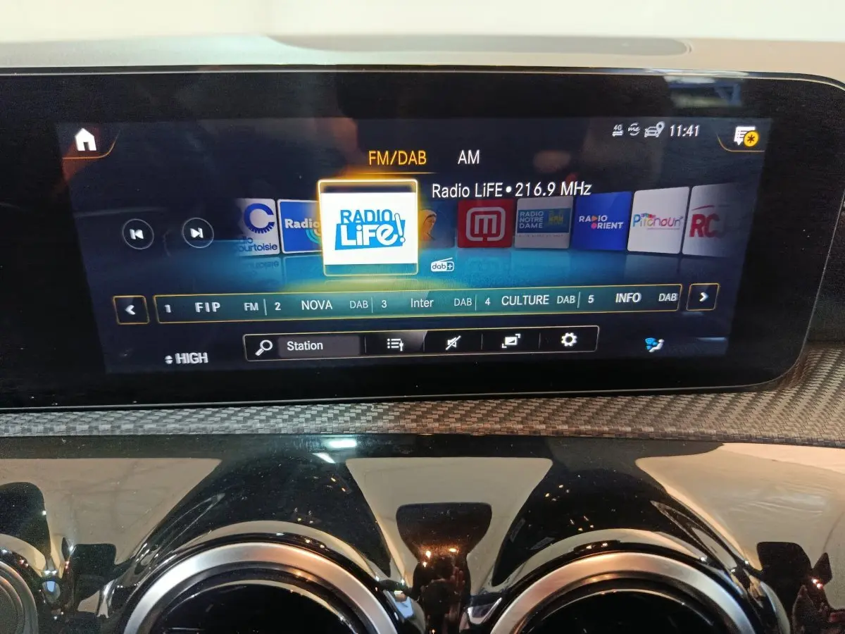 Écran tactile central de la Mercedes Classe A 250 e Business Line 2021 avec affichage radio FM/DAB, entouré de sorties d'air rondes chromées.