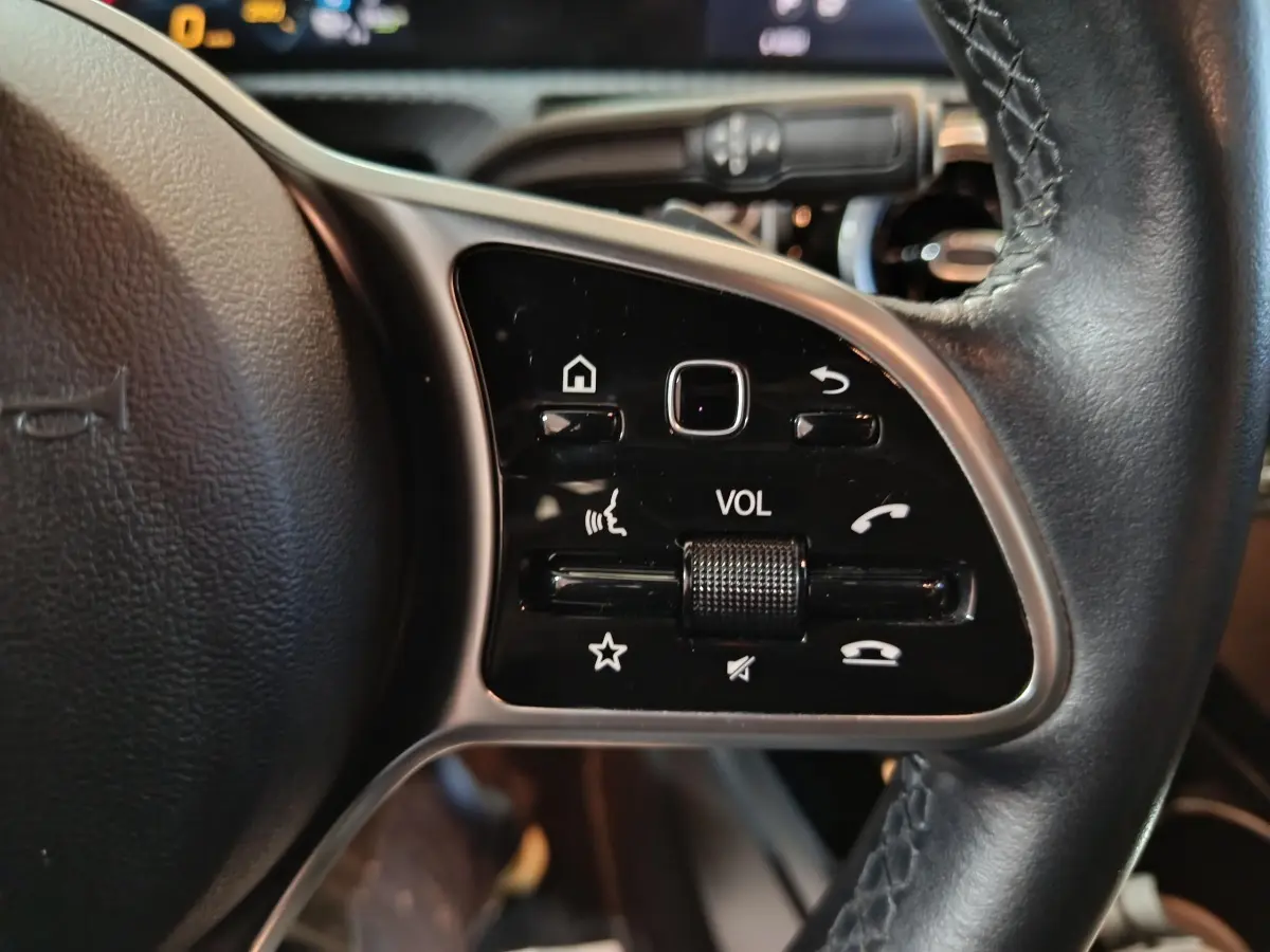 Gros plan sur le volant cuir côté gauche de la Mercedes Classe A 250 e Business Line bleu, avec commandes multifonctions.