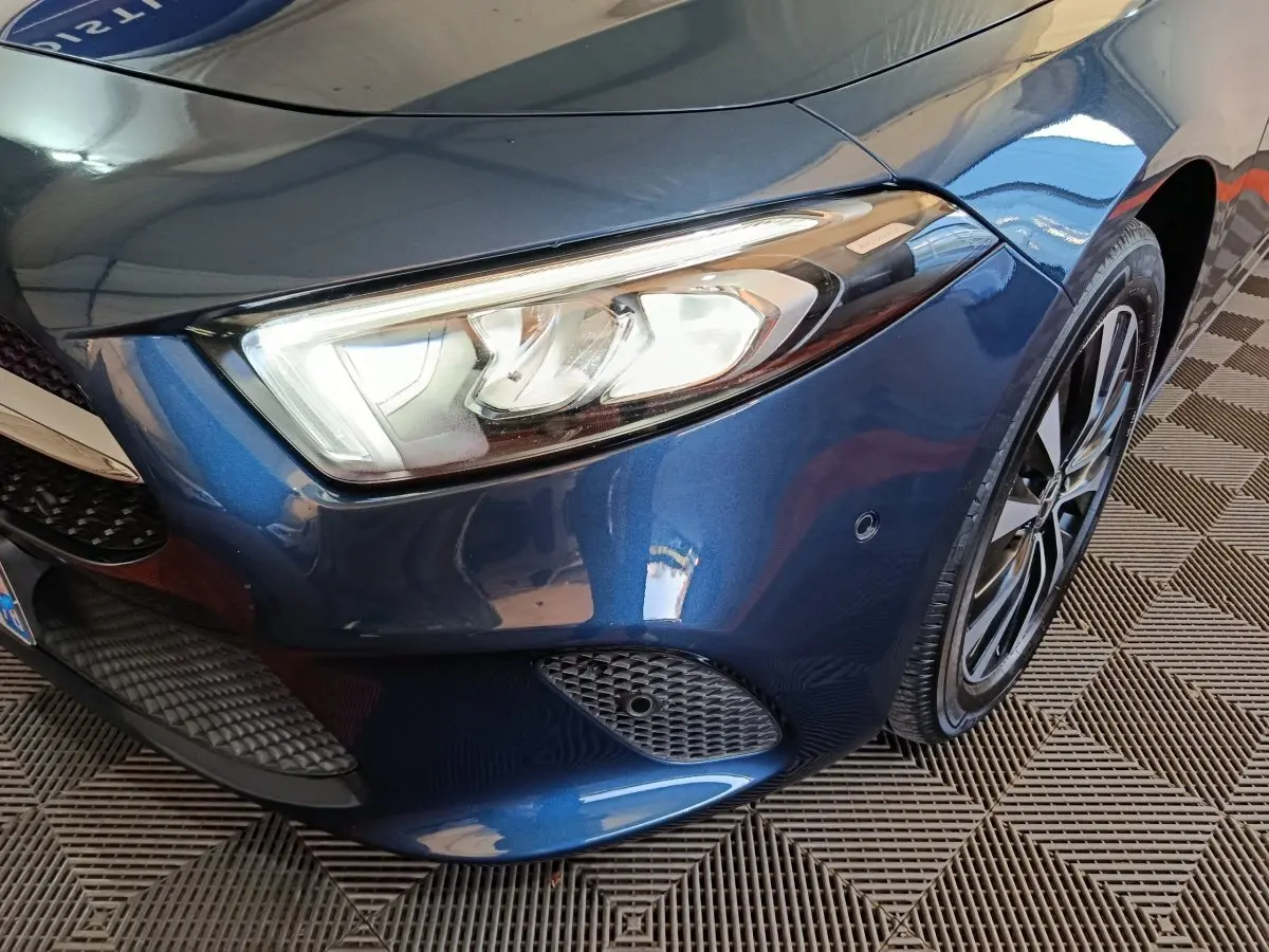 Gros plan sur l'avant droit bleu d'une Mercedes Classe A 250 e Business Line avec phare LED et jante alliage.