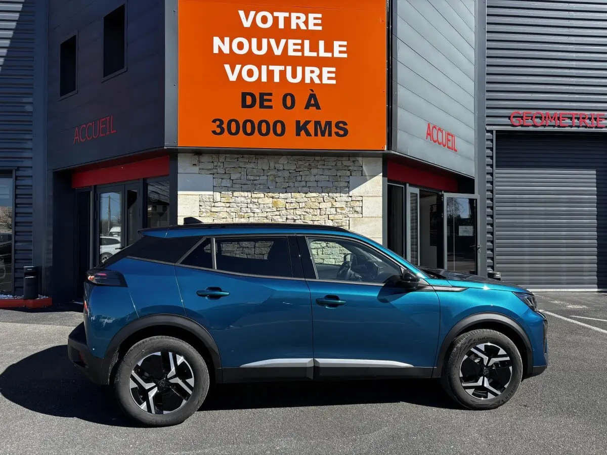 Peugeot 2008 Hybrid 145 e-DCS6 Allure bleu en profil droit, avec jantes noires et toit noir, devant un bâtiment commercial.
