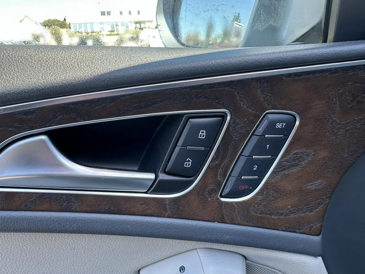 Gros plan sur la porte intérieure côté gauche d’une Audi A6 2015 avec insert bois et commandes de verrouillage et mémoire sièges.
