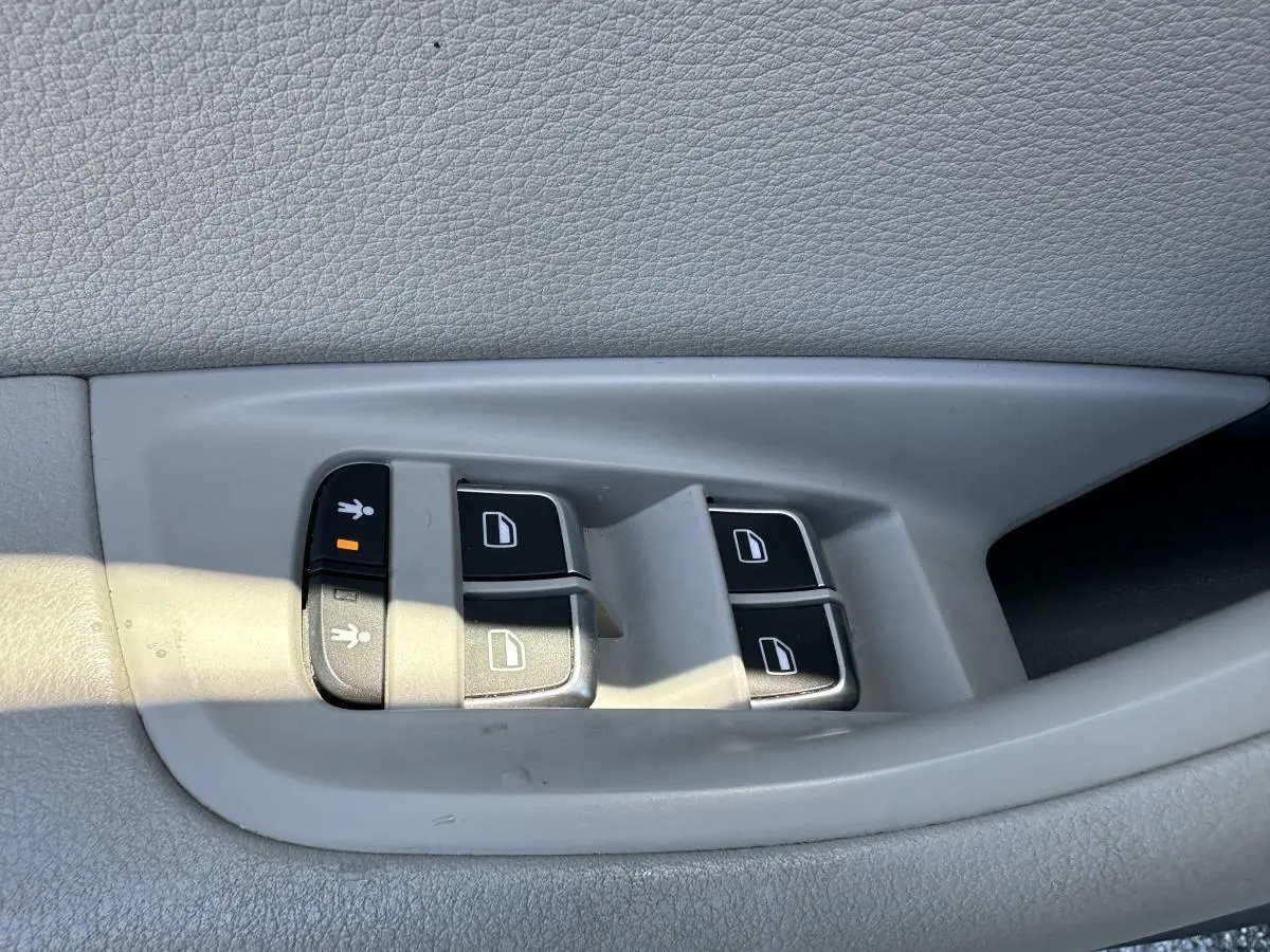 Gros plan sur les commandes de lève-vitres et verrouillage enfant sur la porte intérieure grise d'une Audi A6 2015.