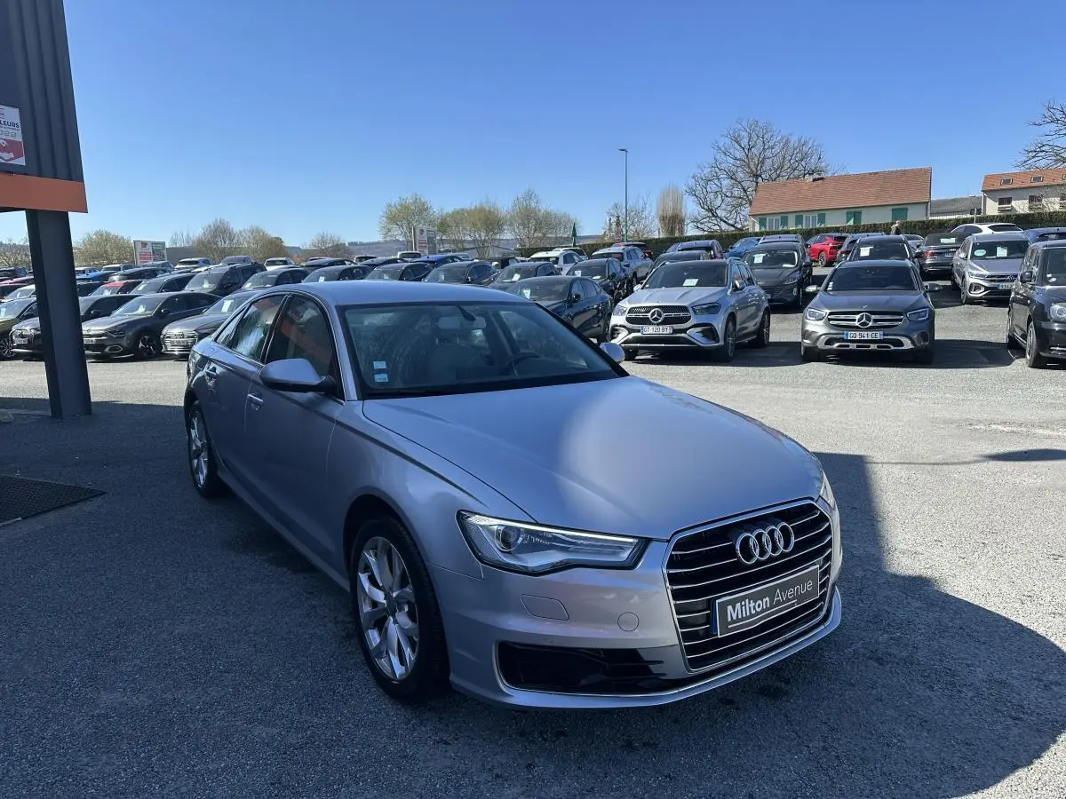 Audi A6 gris vue 3/4 avant droit sur parking avec calandre Singleframe chromée et jantes aluminium.