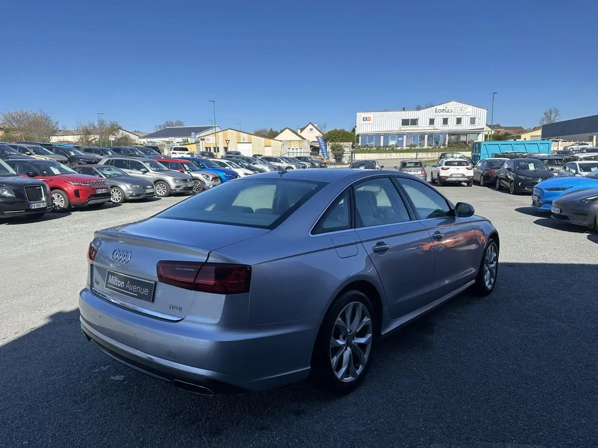 Audi A6 gris vue 3/4 arrière droit sur parking avec jantes aluminium et feux arrière foncés.