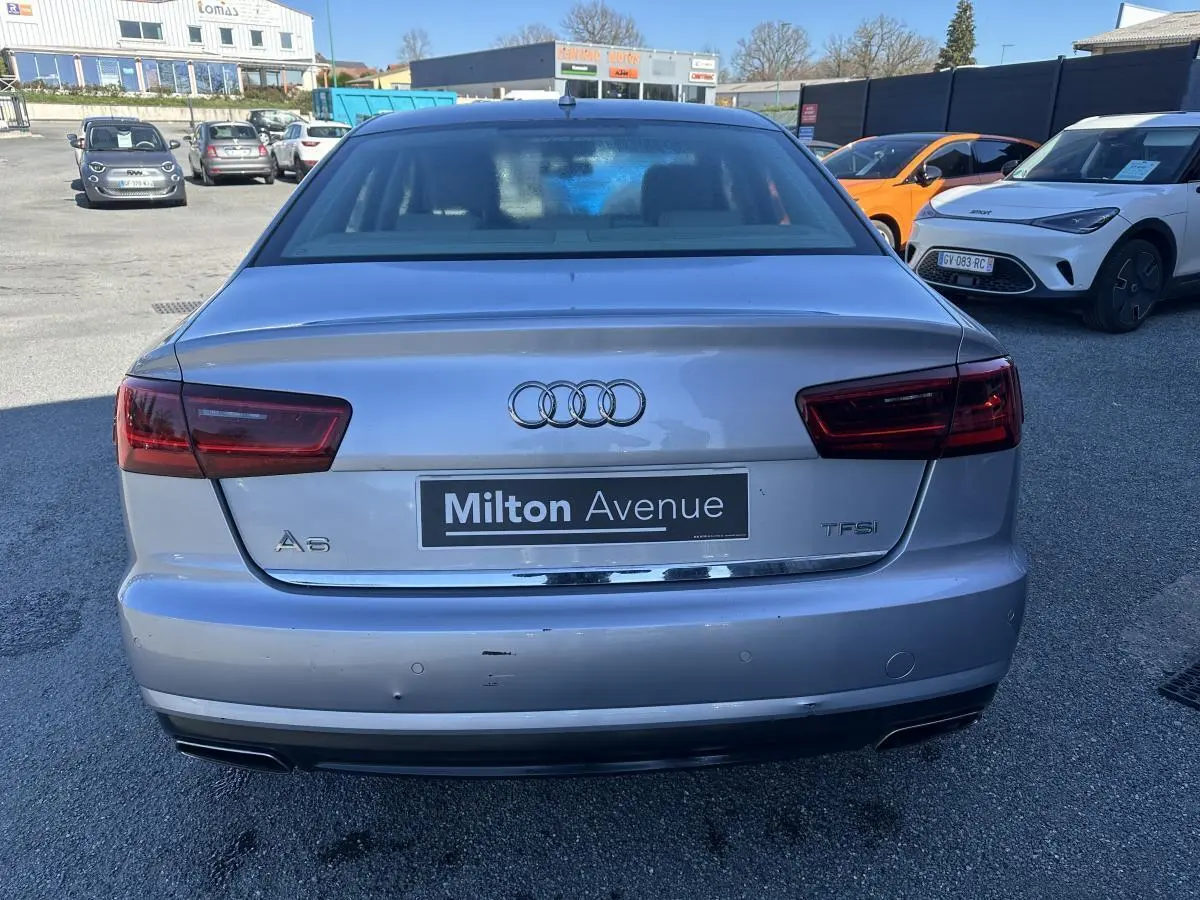 Vue arrière d'une Audi A6 gris métallisé avec logo et badges TFSI, stationnée sur un parking extérieur.