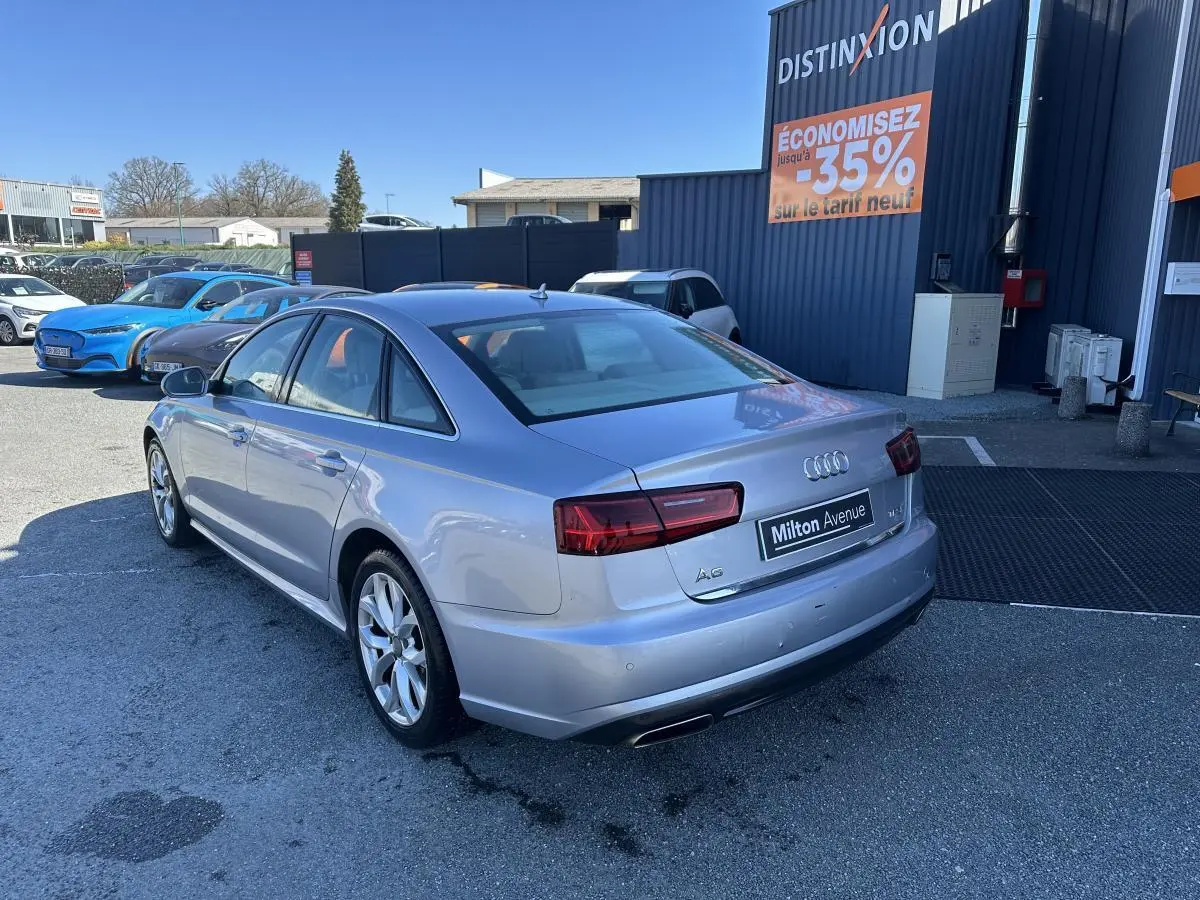 Audi A6 gris vue 3/4 arrière droit, avec feux arrière LED et double sortie d’échappement chromée.