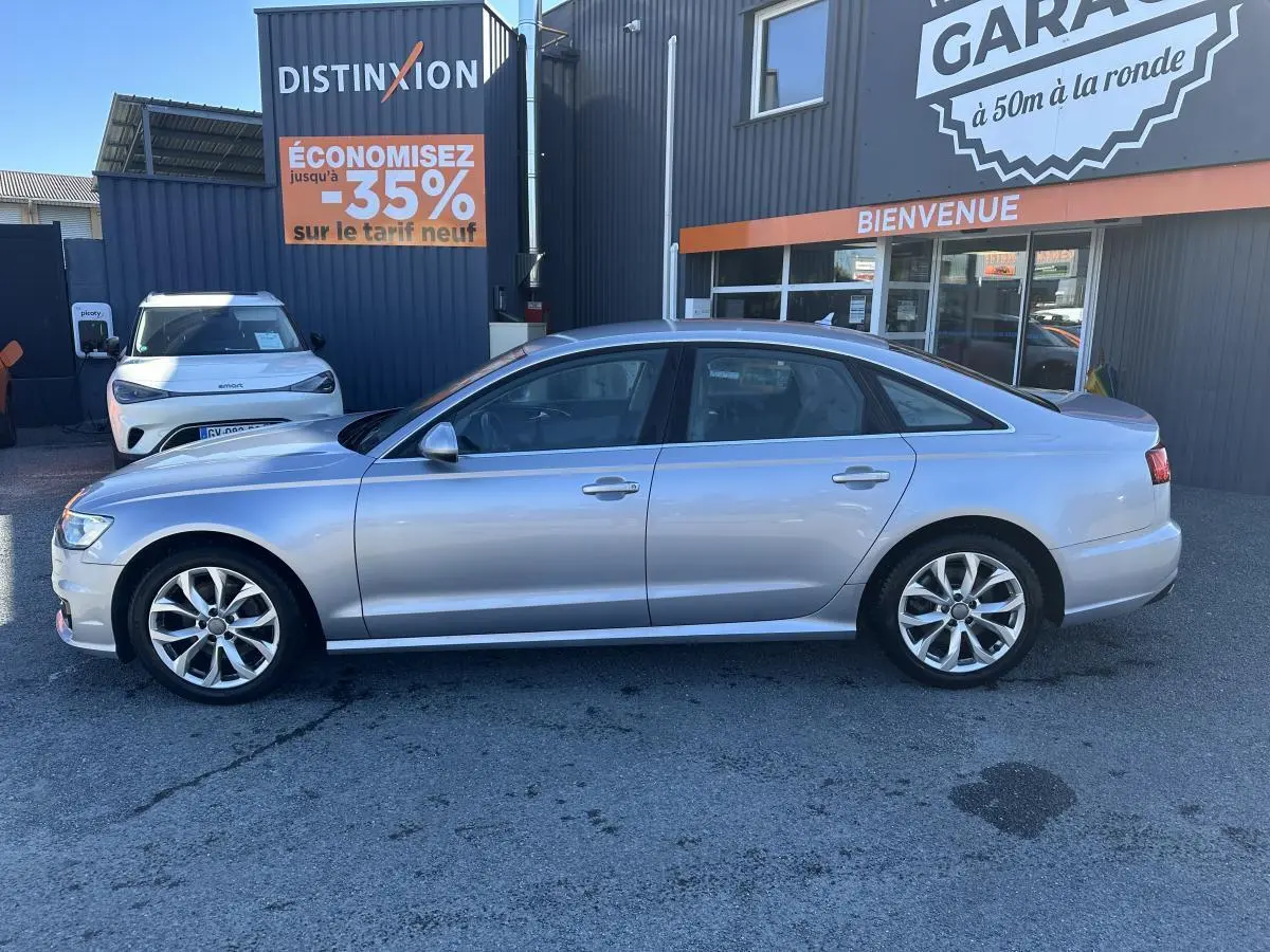 Audi A6 gris en profil droit, garée devant un bâtiment commercial avec enseigne "Distinxion".