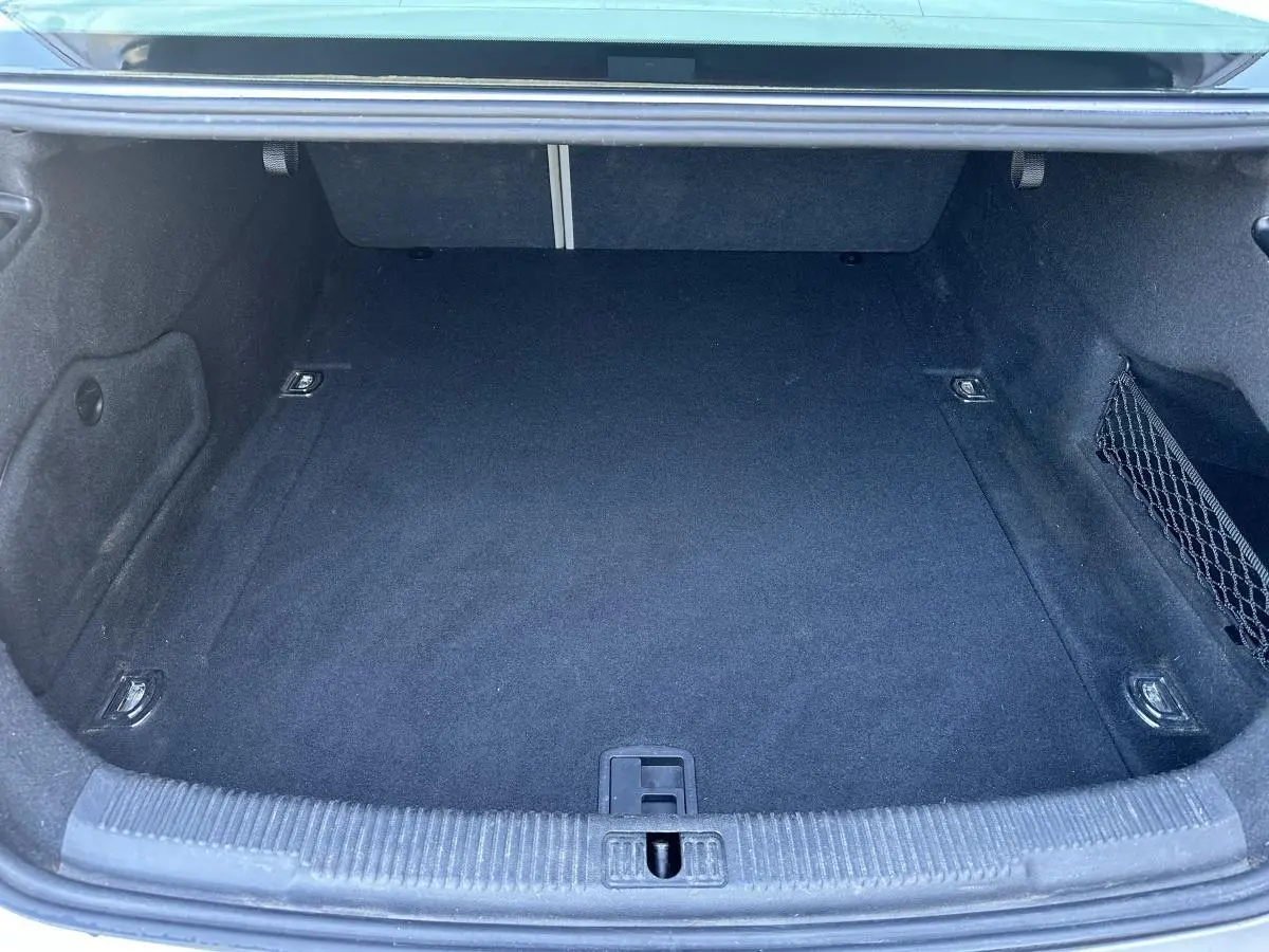Coffre ouvert de l'Audi A6 gris, vue intérieure montrant un espace de rangement propre et vide avec filet latéral.