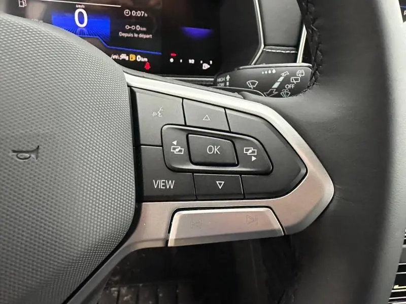 Gros plan sur les commandes au volant cuir noir du Volkswagen T-Cross 2026, avec écran digital en arrière-plan.