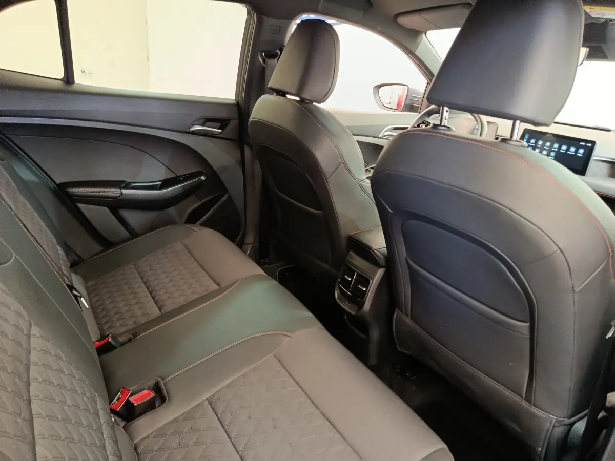 Vue intérieure arrière côté droit du MG3 2024, sièges noirs avec surpiqûres rouges et écran tactile avant visible.