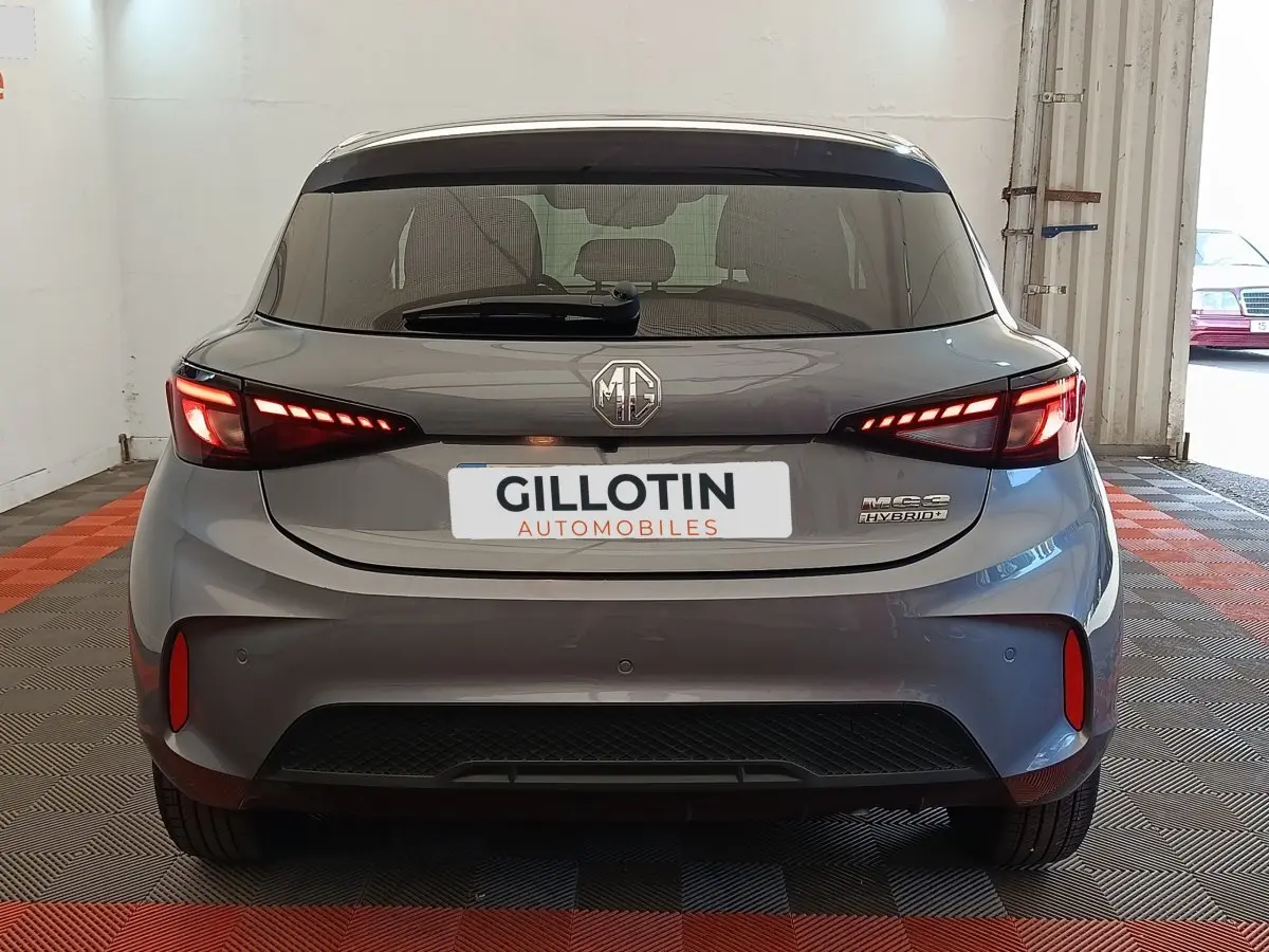 Vue arrière d'une MG3 gris foncé avec feux LED allumés et logo MG visible sur un sol à damiers rouges et gris.