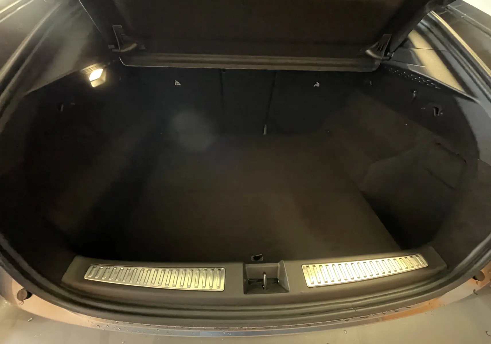 Coffre ouvert vu de l'arrière d'une Renault Rafale Esprit Alpine E-Tech 200 gris schiste, intérieur sombre et éclairé.