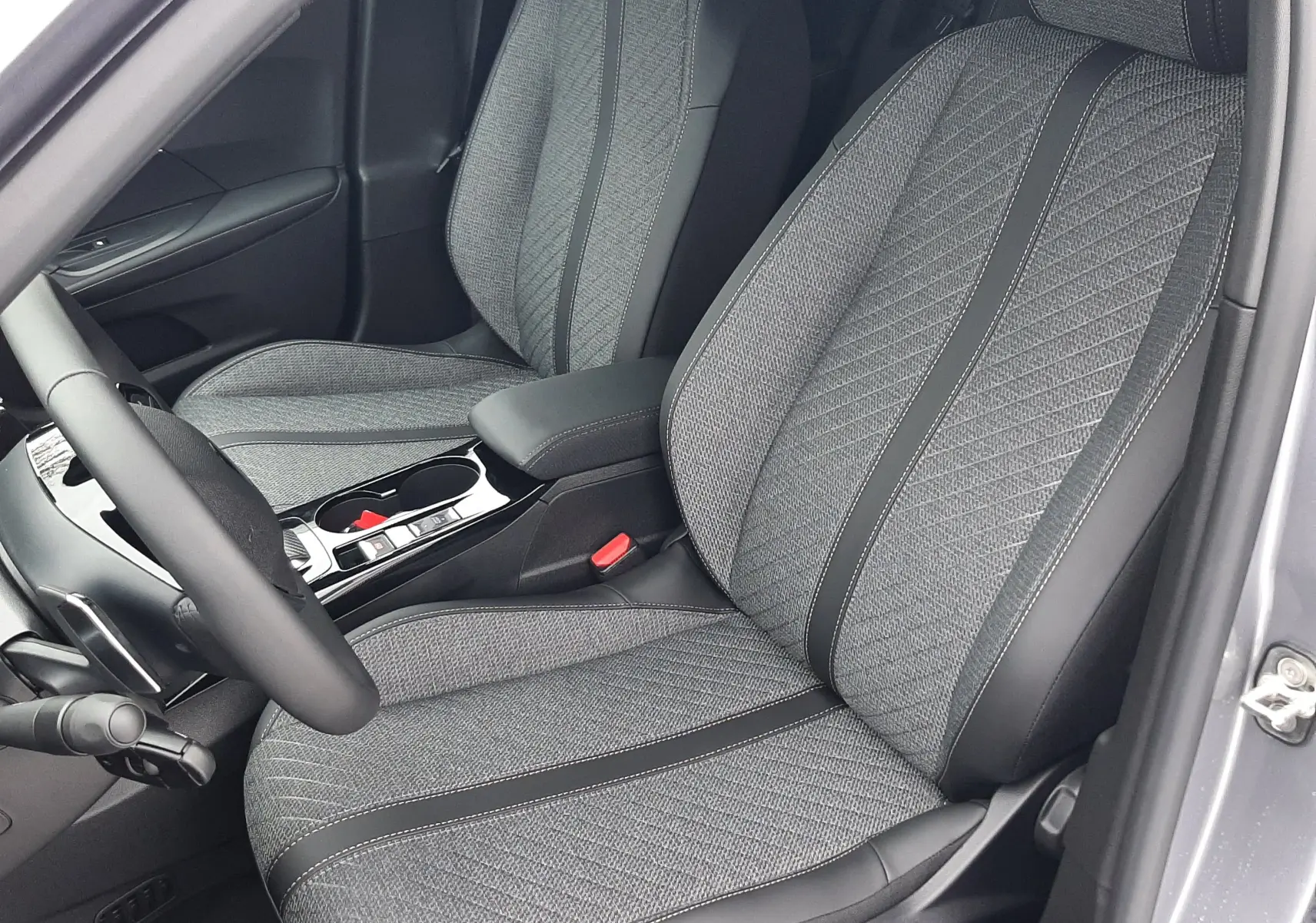 Vue intérieure côté conducteur du PEUGEOT 2008 gris Artense, sièges tissu gris avec surpiqûres et console centrale noire brillante.
