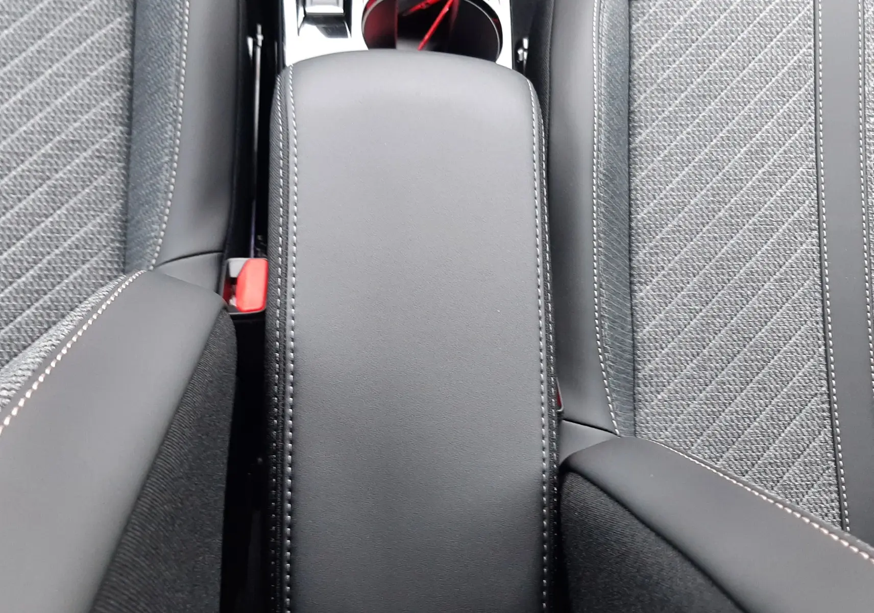 Gros plan sur l'accoudoir central noir et les sièges gris tissu avec surpiqûres blanches dans un Peugeot 2008 hybride 2025.
