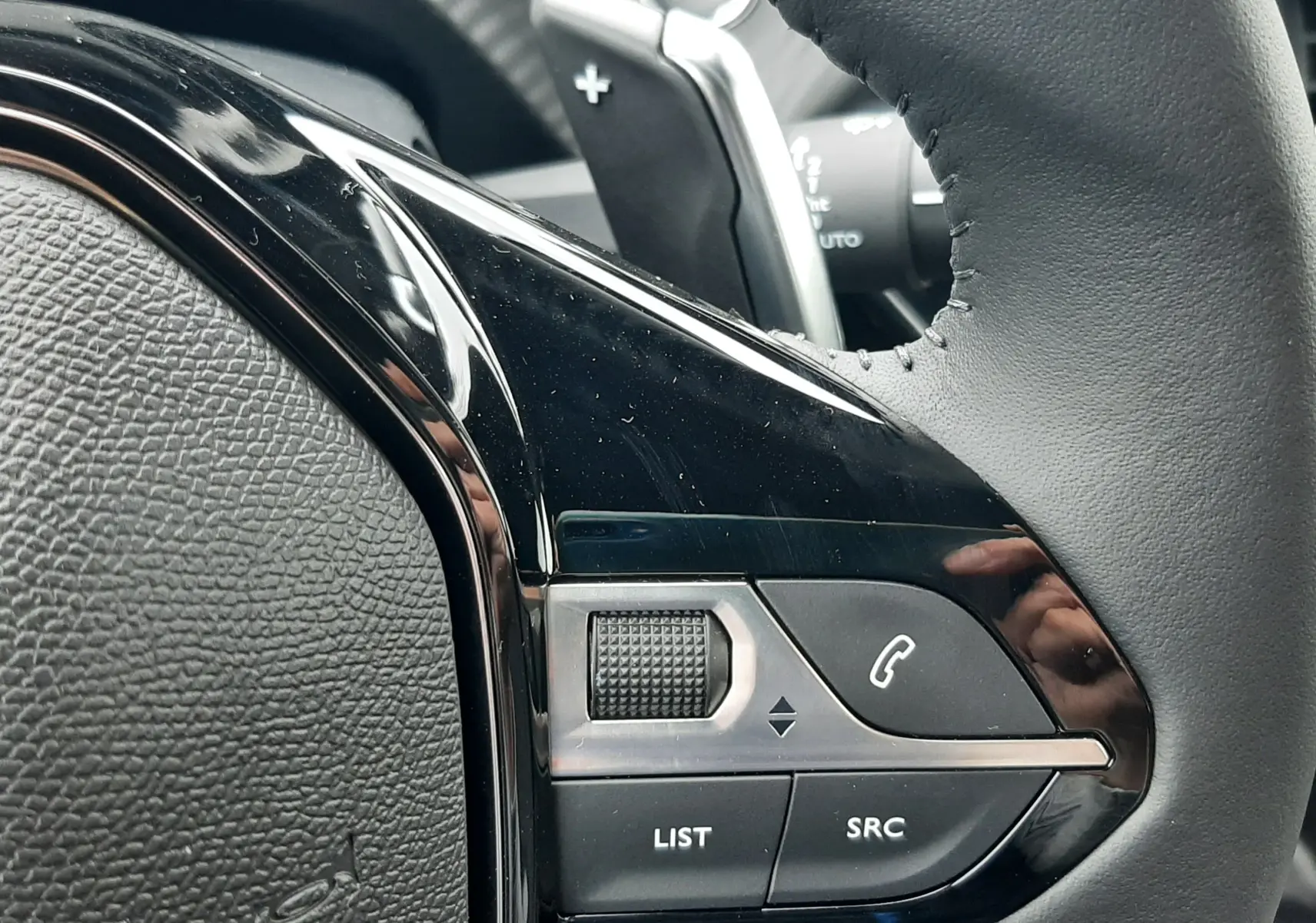 Gros plan sur les commandes noires du volant en cuir du Peugeot 2008 gris Artense, version hybride 2025.