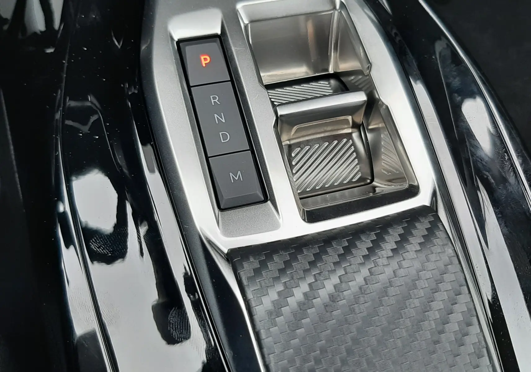 Gros plan sur la commande de boîte automatique avec bouton P rouge et surface effet carbone dans un Peugeot 2008 gris Artense.