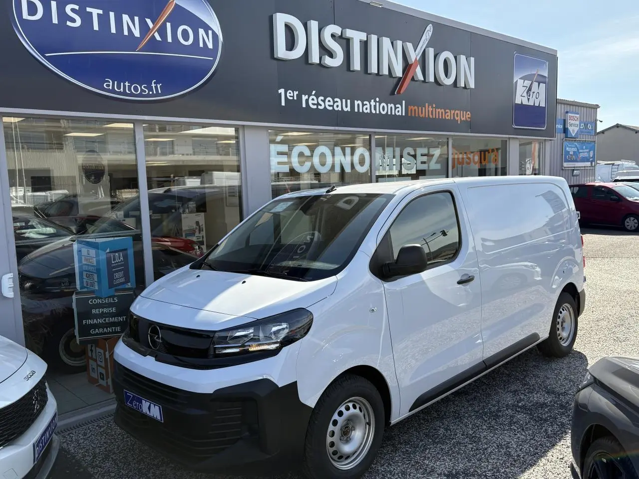 Vue 3/4 avant droite d’un Opel Vivaro blanc 2024 utilitaire avec calandre noire et jantes acier, devant un concessionnaire.