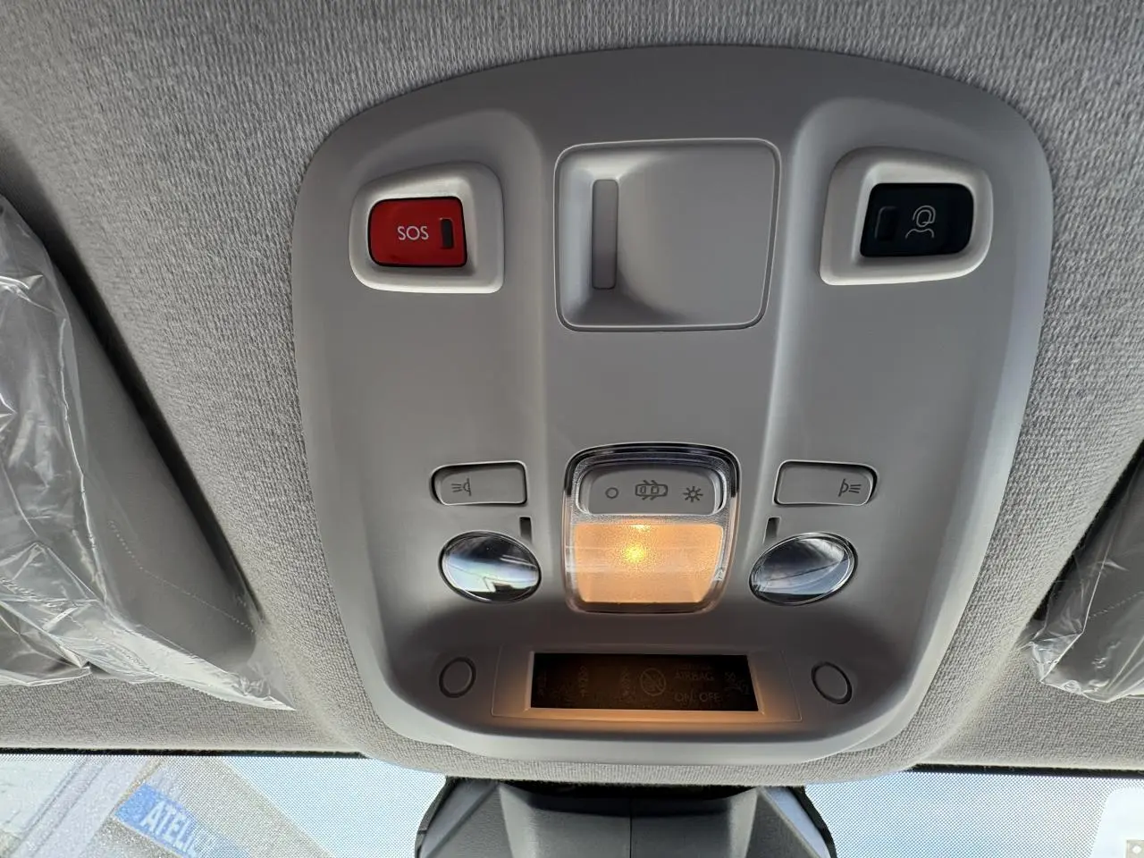 Vue en contre-plongée du plafonnier gris clair avec boutons SOS et éclairage intérieur allumé dans un Opel Vivaro blanc 2024.
