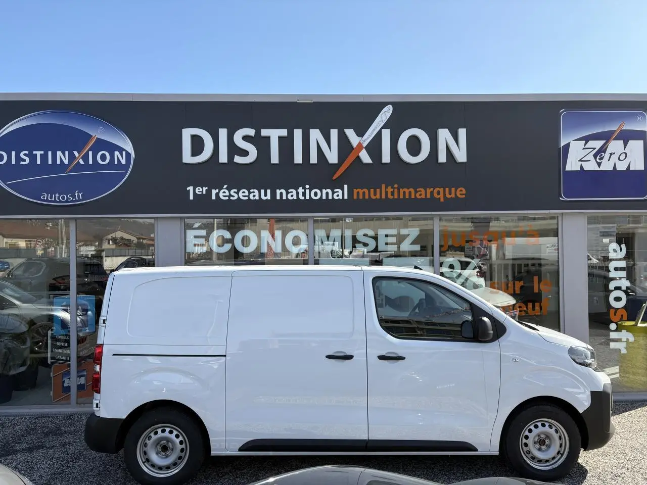 Profil droit d’un utilitaire Opel Vivaro blanc 2024 stationné devant une concession Distinxion.