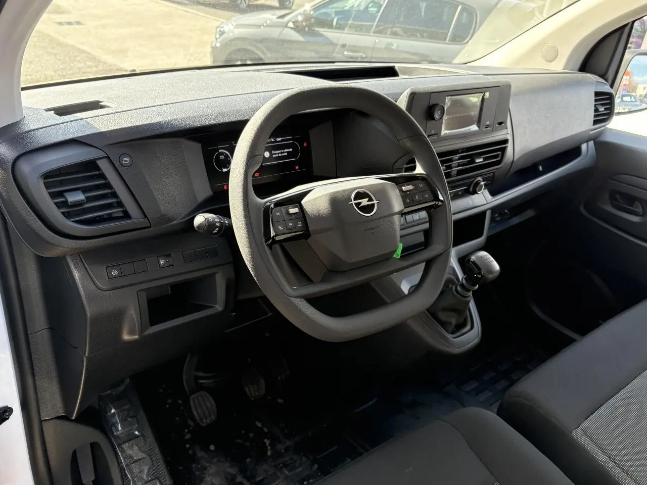 Vue intérieure côté conducteur de l'Opel Vivaro 2024, tableau de bord noir avec volant multifonction et boîte manuelle.