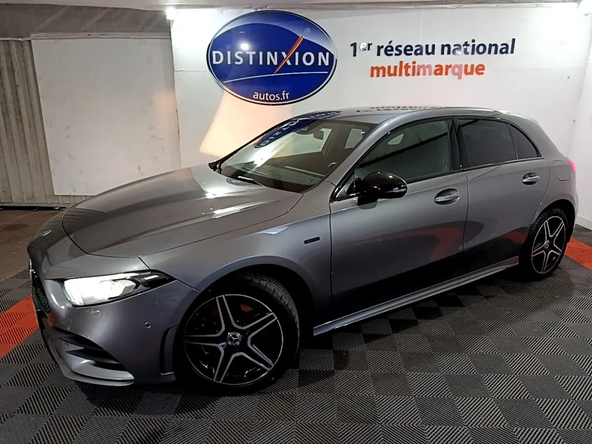 Vue 3/4 avant droit d'une Mercedes Classe A 250 e AMG Line gris foncé avec jantes alliage noires et phares LED allumés.