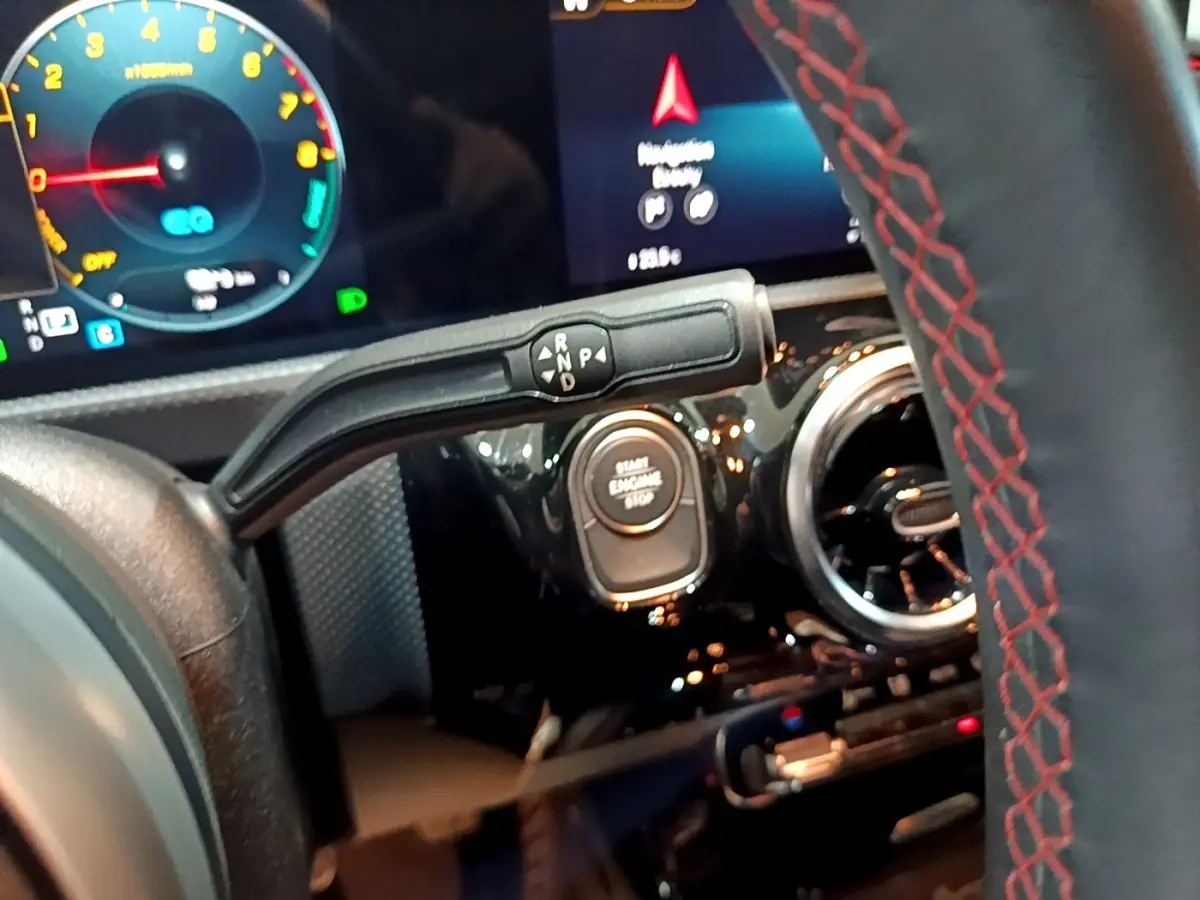 Vue rapprochée du volant cuir avec surpiqûres rouges et levier de vitesses sur tableau de bord noir brillant d'une Mercedes Classe A.