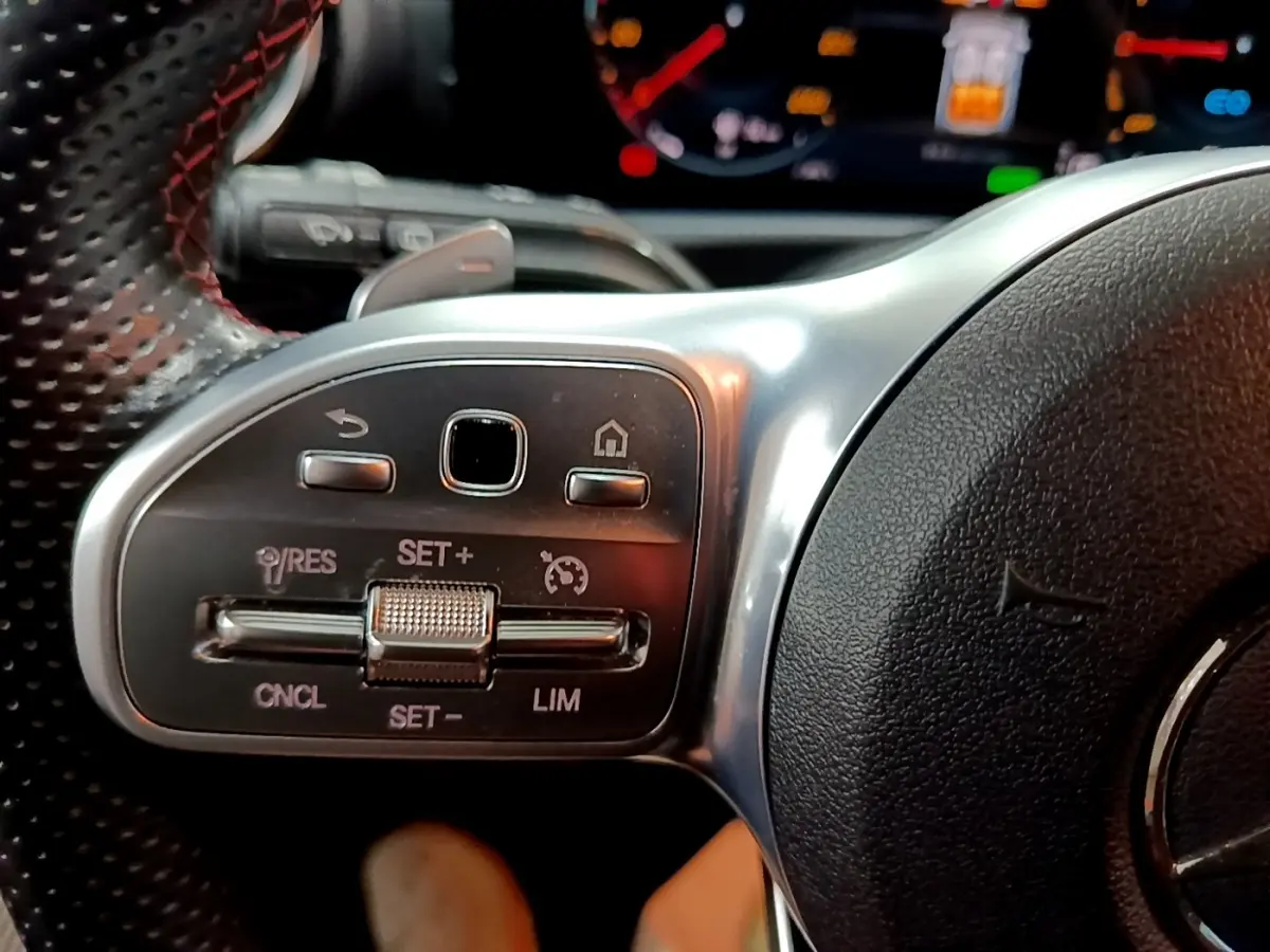 Gros plan sur le côté gauche du volant cuir et alu de la Mercedes Classe A 250 e AMG Line avec commandes multifonctions.