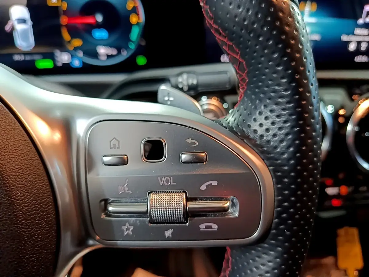 Gros plan sur le volant cuir et alu avec commandes multifonctions de la Mercedes Classe A 250 e AMG Line gris foncé.