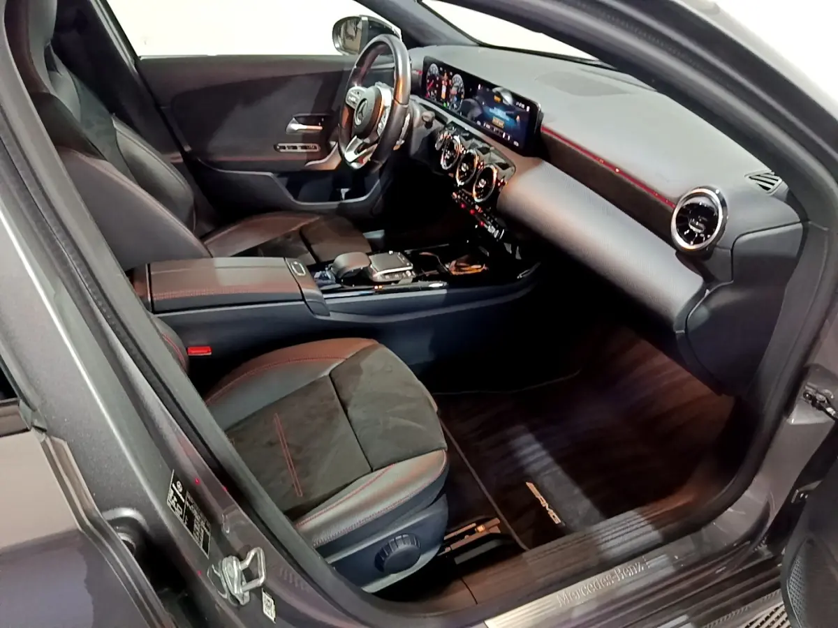 Vue intérieure côté conducteur de la Mercedes Classe A 250 e AMG Line 2021, sièges noirs avec surpiqûres rouges et tableau de bord numérique.