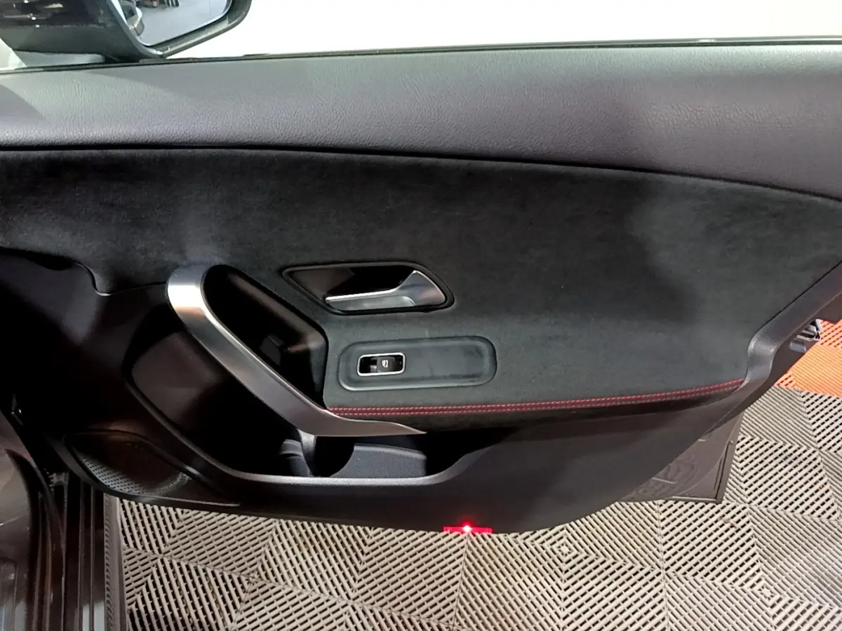 Vue intérieure du panneau de porte côté gauche de la Mercedes Classe A 250 e AMG Line gris foncé avec surpiqûres rouges et poignée alu.