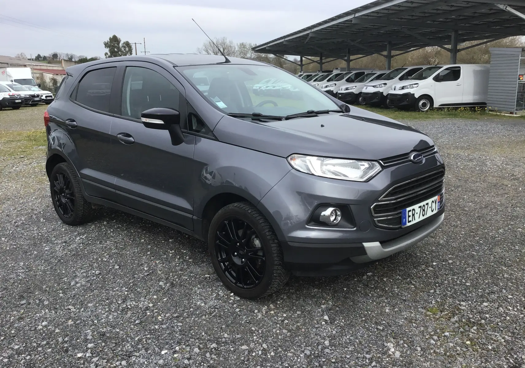 Ford EcoSport gris foncé métal vu en 3/4 avant droit, avec jantes noires et calandre chromée, sur parking extérieur.