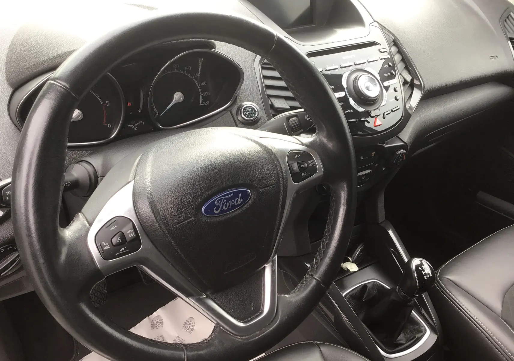 Vue intérieure centrée sur le volant Ford et la console centrale noire du Ford Ecosport gris foncé, avec levier de vitesse manuel visible.