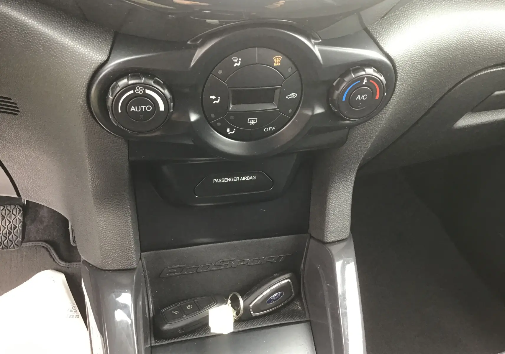 Vue rapprochée du tableau de bord central du Ford EcoSport gris foncé, avec commandes de climatisation et clés mains libres posées.