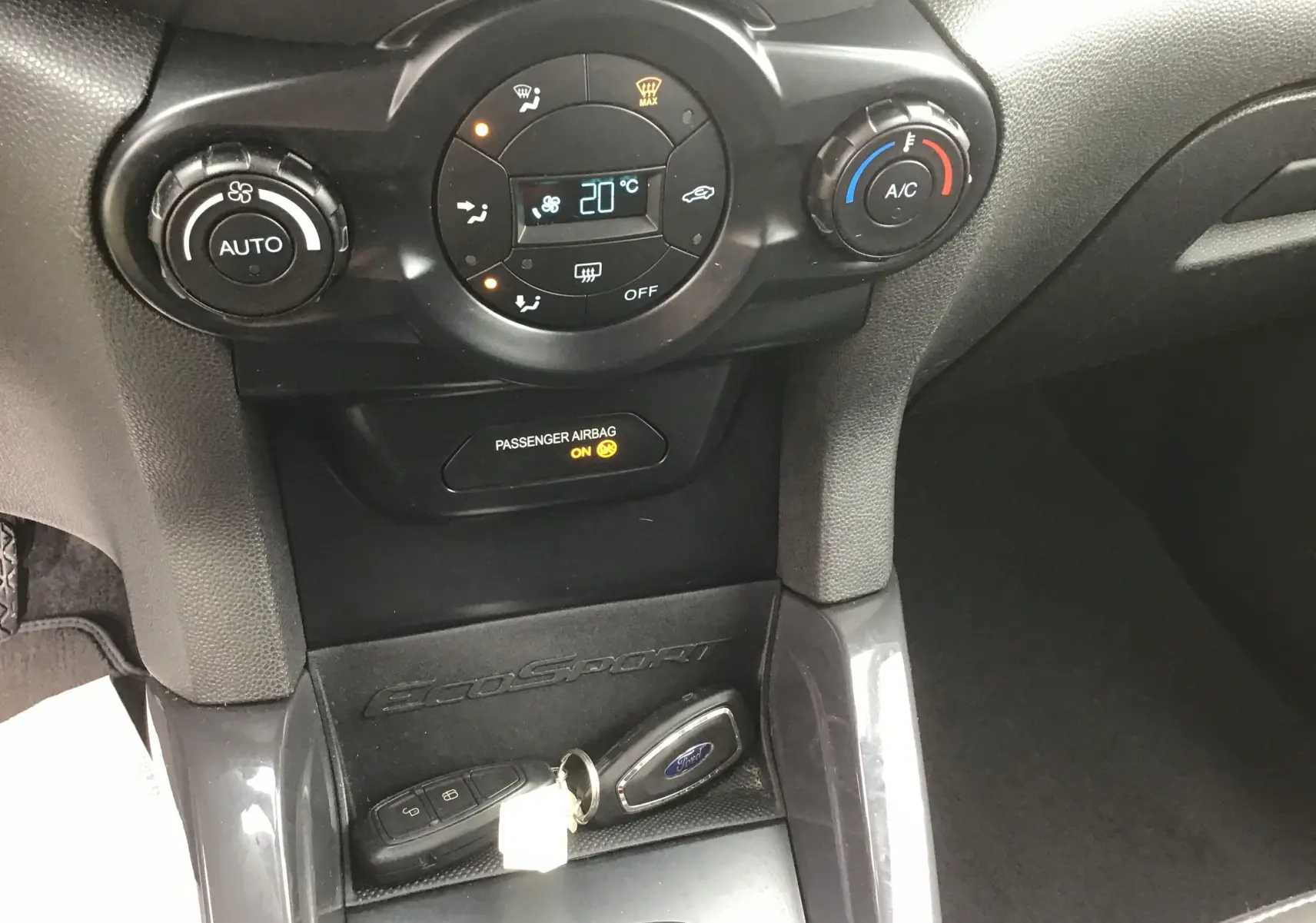 Gros plan sur la console centrale du Ford EcoSport gris foncé, montrant la climatisation digitale et la clé mains libres.