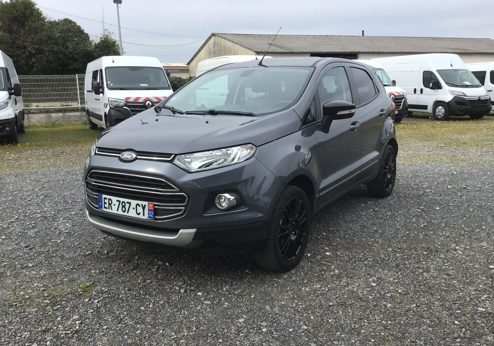 Ford Ecosport gris foncé métal vu en 3/4 avant droit, avec jantes noires et calandre chromée sur parking extérieur.