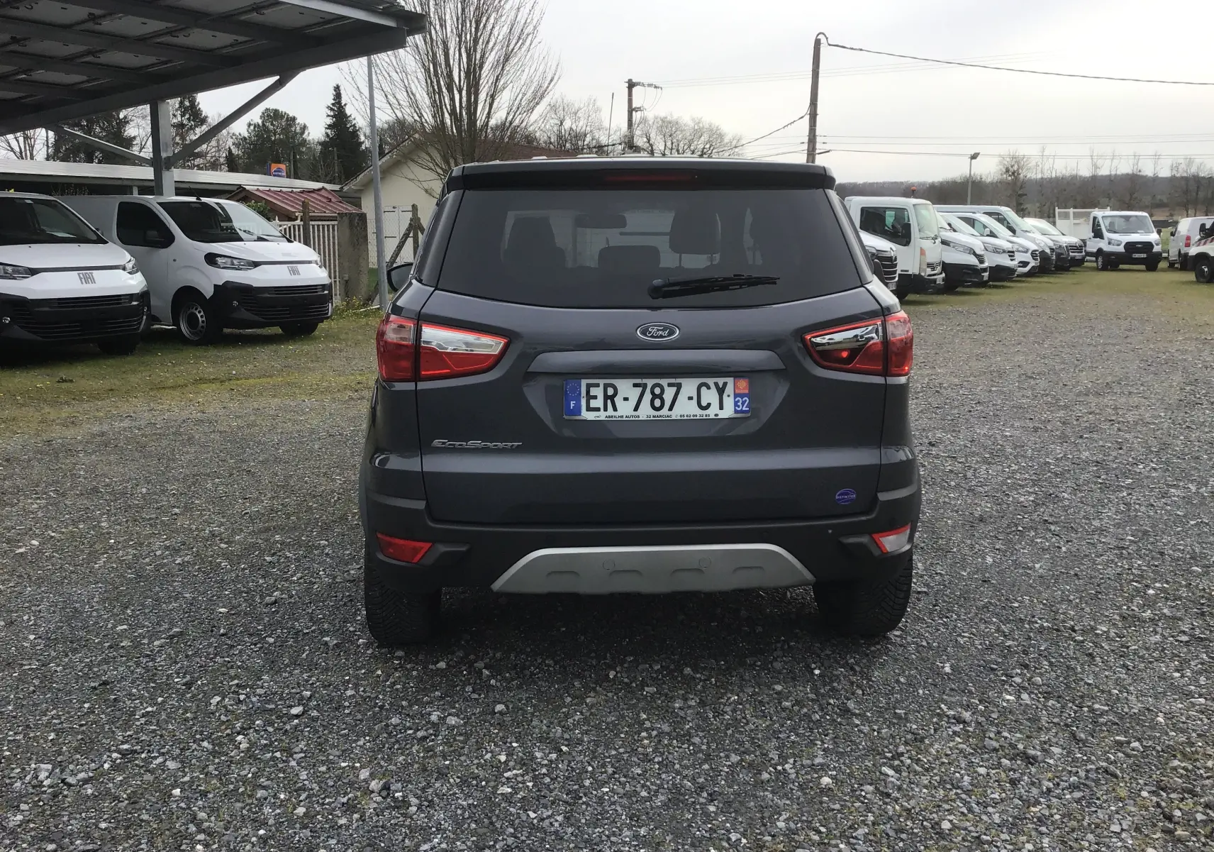 Vue arrière d'un Ford EcoSport gris foncé métallisé, avec plaques d'immatriculation françaises, sur un sol gravillonné.