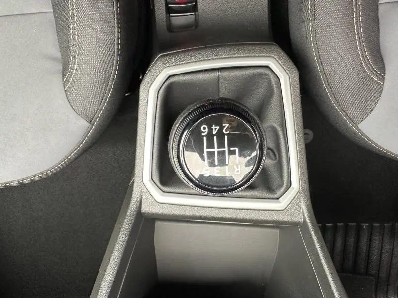 Vue plongeante sur le levier de vitesses manuel noir entouré de garniture grise, entre les sièges tissu gris du Dacia Jogger.