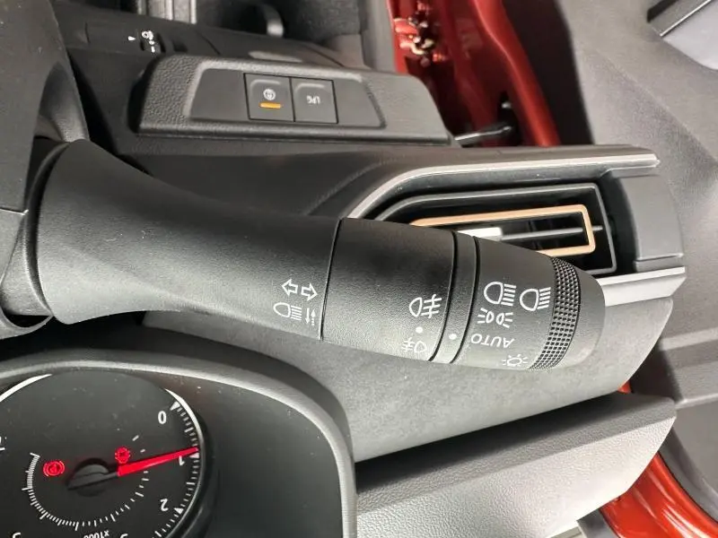 Gros plan sur la commande des feux et clignotants à gauche du volant dans un intérieur noir avec détails brun Terracota métallisé.