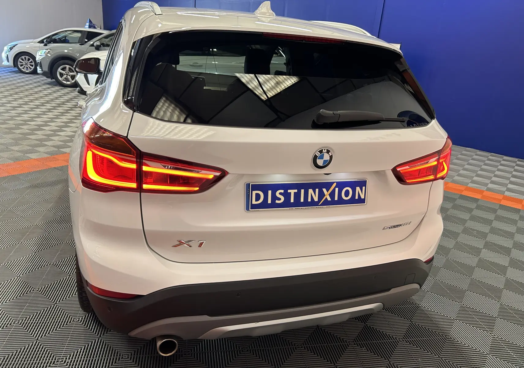 Vue arrière droite d'un BMW X1 blanc avec feux allumés et hayon électrique dans un showroom.