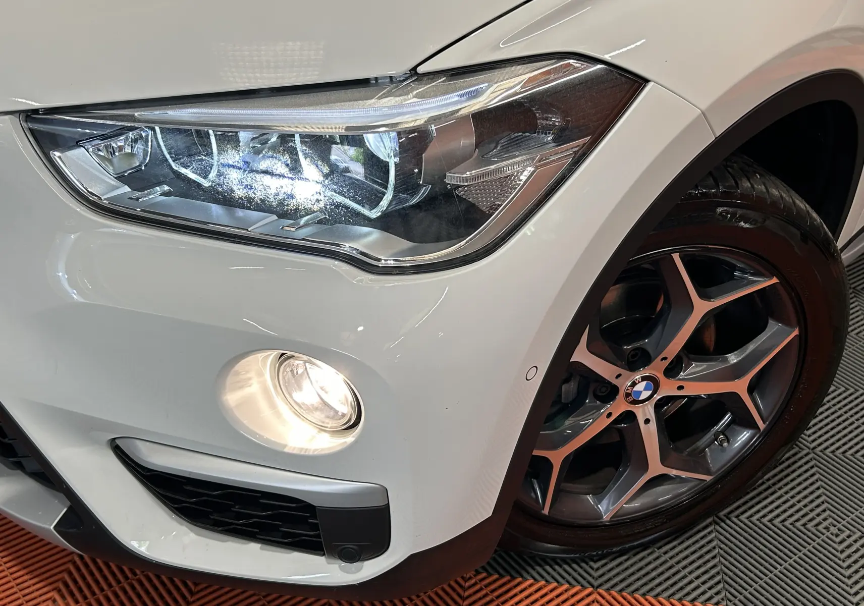 Gros plan sur l'avant droit blanc du BMW X1 sDrive18iA 2018, avec phare LED allumé et jante alliage distinctive.