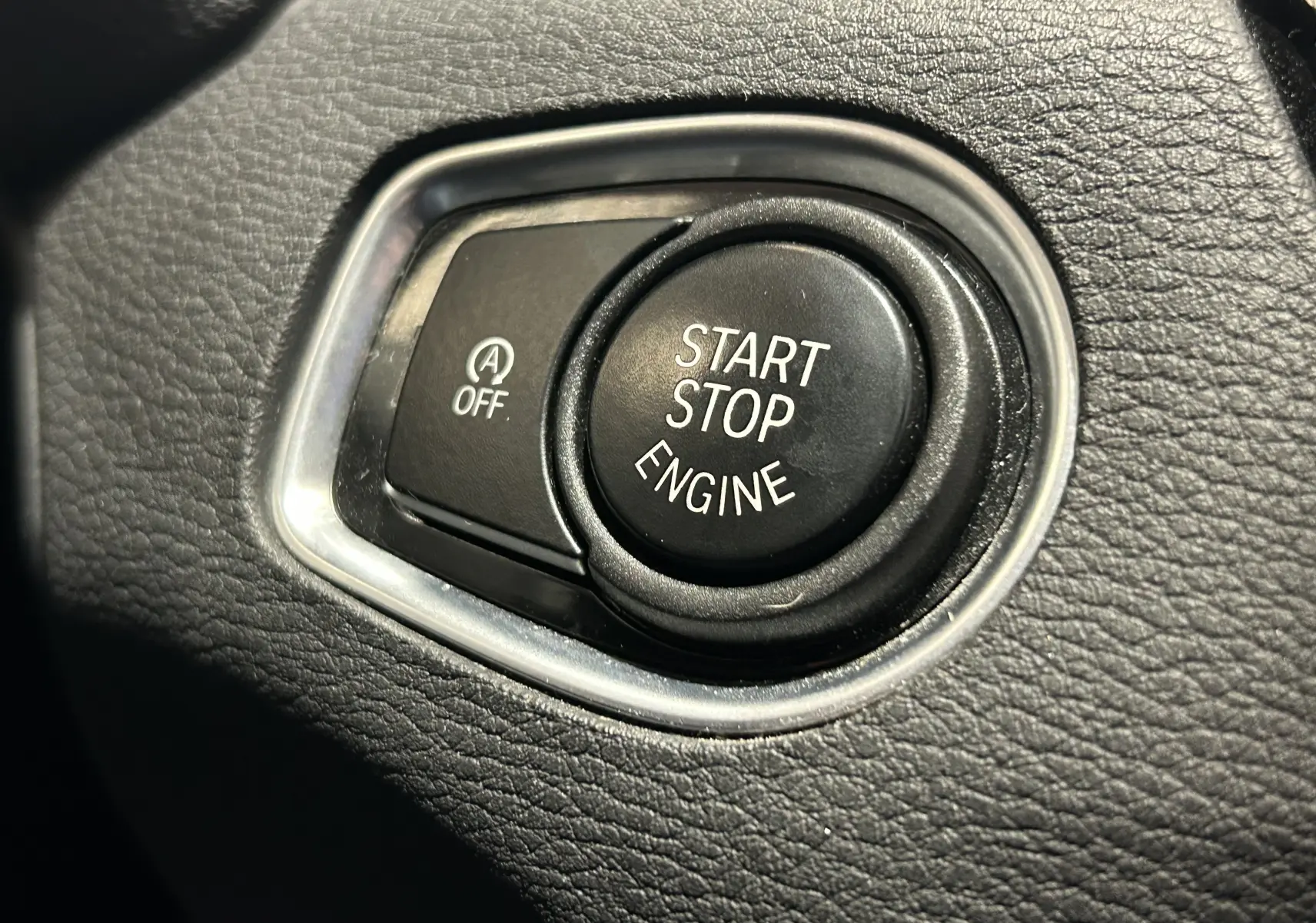 Gros plan sur le bouton Start Stop Engine noir entouré de cuir noir texturé dans une BMW X1 2018.