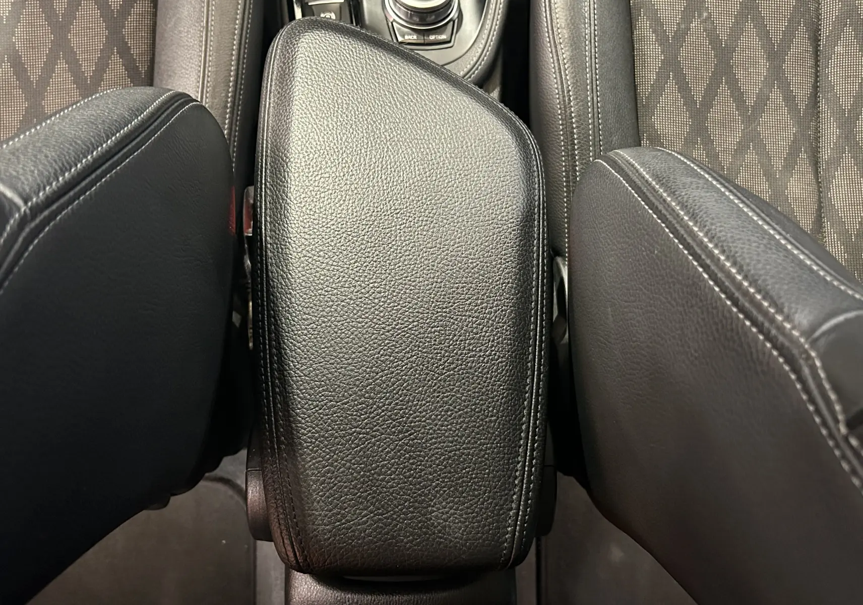 Gros plan sur l'accoudoir central en cuir noir entre les sièges avant à tissu gris à motifs du BMW X1 blanc.