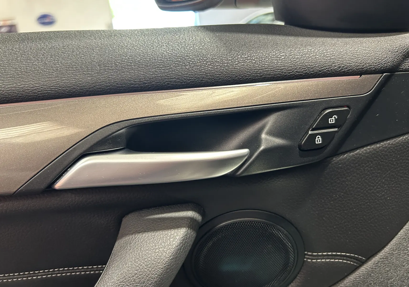 Poignée intérieure côté gauche de la porte avant d'une BMW X1 blanche, avec boutons de verrouillage et haut-parleur visible.