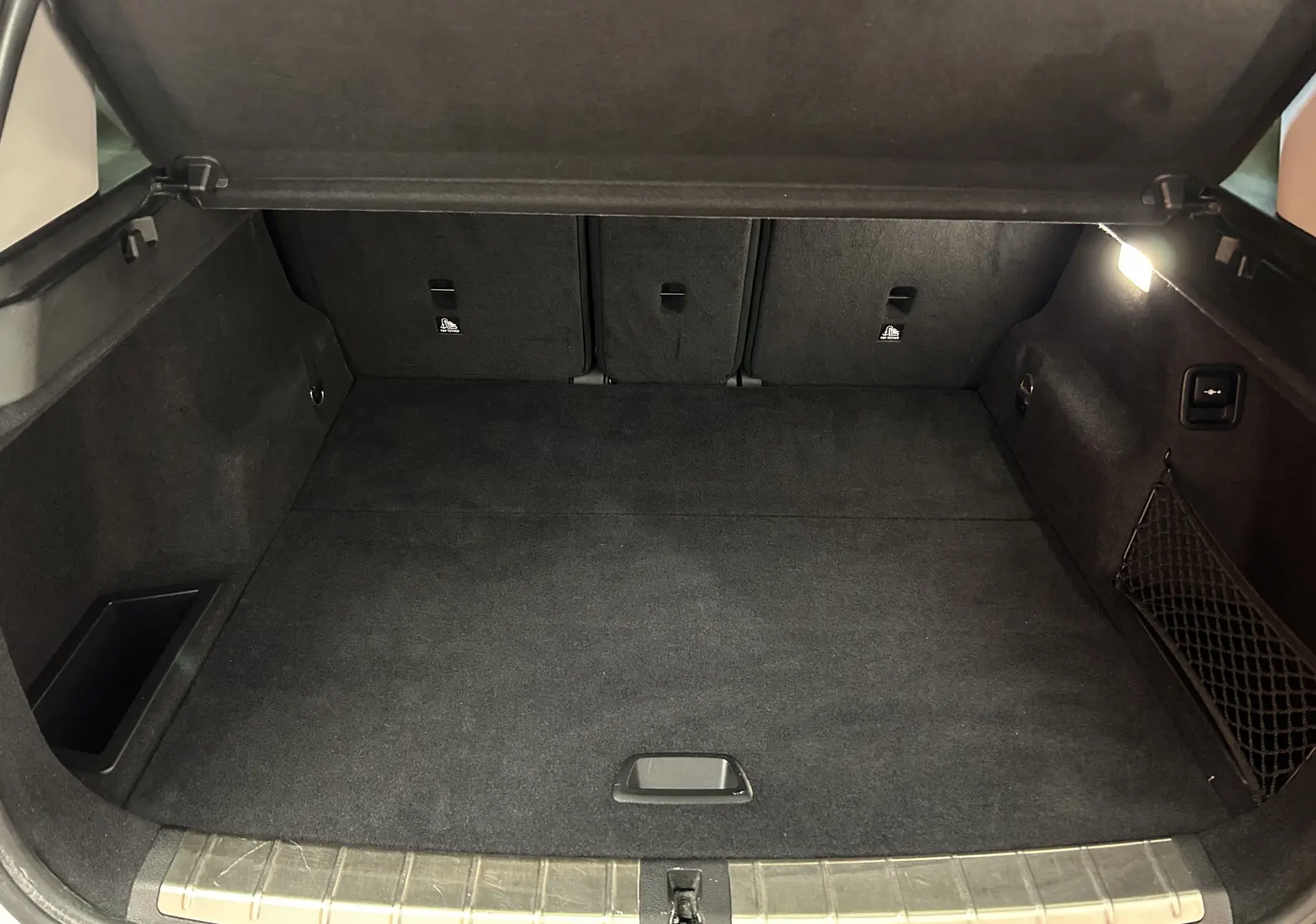 Coffre ouvert vu de l'arrière d'un BMW X1 blanc, montrant un espace de chargement propre et bien éclairé.
