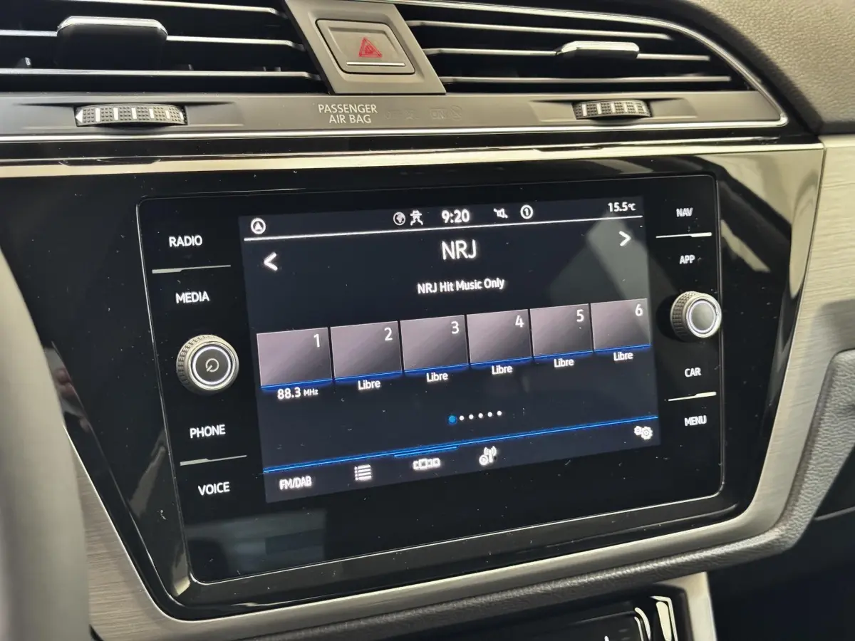 Gros plan sur l’écran tactile central du Volkswagen Touran bleu 2024 affichant la radio NRJ.